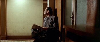 Movie still from “Nikita” (1990), directed by Luc Besson – A man sitting in a chair holding a newspaper; Medium shot, Low angle