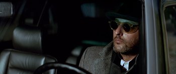Movie still from “Nikita” (1990), directed by Luc Besson – A man in a hat and sunglasses sitting in a car; Close Up shot, Low angle