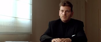 Movie still from “Nikita” (1990), directed by Luc Besson – A person sitting at a table wearing a suit; Close Up shot, Low angle