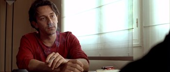 Movie still from “Nikita” (1990), directed by Luc Besson – A person sitting at a table smoking a cigarette; Close Up shot, Low angle