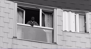 Movie still from “La haine” (1995), directed by Mathieu Kassovitz – A man standing in a window looking out of a window; Medium shot, Low angle
