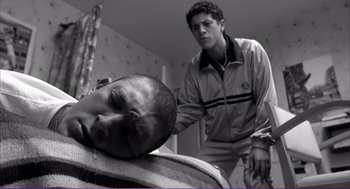 Movie still from “La haine” (1995), directed by Mathieu Kassovitz – A man standing next to another man in a room; Medium shot, Low angle