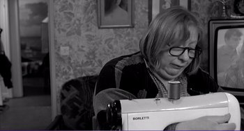 Movie still from “La haine” (1995), directed by Mathieu Kassovitz – A woman sitting in front of a sewing machine in a living room; Medium shot, High angle