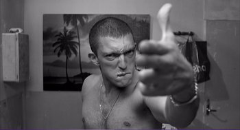 Movie still from “La haine” (1995), directed by Mathieu Kassovitz – A shirtless man giving a thumbs up in front of a palm tree; Medium shot, Low angle