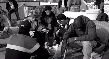 Movie still from “La haine” (1995), directed by Mathieu Kassovitz – A black and white photo of a group of men sitting on a bench; Medium shot, High angle