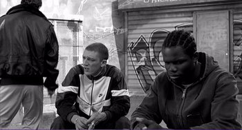 Movie still from “La haine” (1995), directed by Mathieu Kassovitz – A group of young men sitting next to each other on the street; Medium shot, Low angle