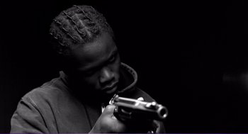 Movie still from “La haine” (1995), directed by Mathieu Kassovitz – A man with dreadlocks is holding a gun in his hands; Close Up shot, Low angle