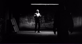 Movie still from “La haine” (1995), directed by Mathieu Kassovitz – A man standing in the dark in front of a wall; Wide shot, Low angle