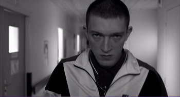 Movie still from “La haine” (1995), directed by Mathieu Kassovitz – A man in a white jacket is standing in a hallway; Medium shot, Low angle