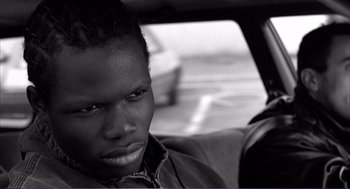 Movie still from “La haine” (1995), directed by Mathieu Kassovitz – A black and white photo of a person in a car; Close Up shot, Low angle