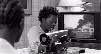 Movie still from “La haine” (1995), directed by Mathieu Kassovitz – A woman sitting in front of a sewing machine in a room; Medium shot, Low angle