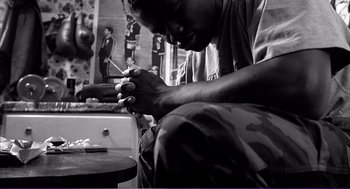 Movie still from “La haine” (1995), directed by Mathieu Kassovitz – A man sitting on the ground with a cigarette in his hand; Medium shot, High angle