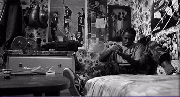 Movie still from “La haine” (1995), directed by Mathieu Kassovitz – A black and white photo of a man sitting in a bedroom; Medium shot, High angle