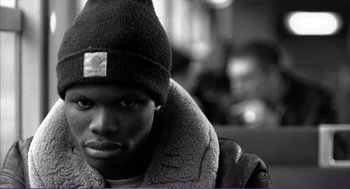 Movie still from “La haine” (1995), directed by Mathieu Kassovitz – A black and white photo of a man wearing a hat; Close Up shot, Low angle