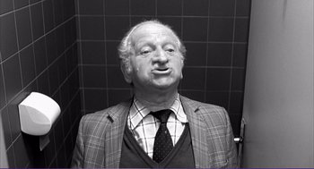 Movie still from “La haine” (1995), directed by Mathieu Kassovitz – An older man wearing a suit and tie in front of a tiled wall; Close Up shot, High angle