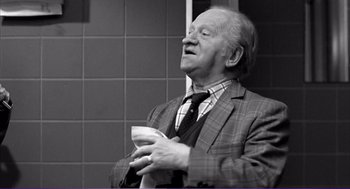 Movie still from “La haine” (1995), directed by Mathieu Kassovitz – An older man holding a cup in his hands; Medium shot, Low angle
