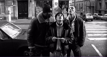 Movie still from “La haine” (1995), directed by Mathieu Kassovitz – A group of young men standing next to each other on the street; Medium shot, Low angle