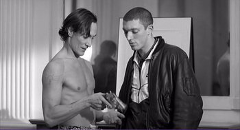Movie still from “La haine” (1995), directed by Mathieu Kassovitz – Two men are looking at a pair of headphones; Medium shot, Low angle
