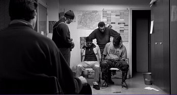 Movie still from “La haine” (1995), directed by Mathieu Kassovitz – A group of men sitting in a room next to each other; Wide shot, High angle