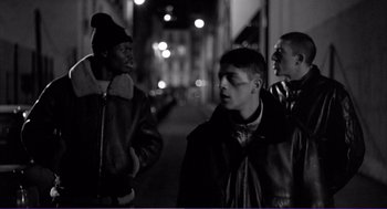Movie still from “La haine” (1995), directed by Mathieu Kassovitz – A group of young men standing next to each other on a sidewalk; Medium shot, Over the shoulder angle