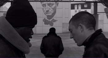 Movie still from “La haine” (1995), directed by Mathieu Kassovitz – Two young men standing next to each other in front of a mural; Medium shot, Over the shoulder angle