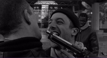 Movie still from “La haine” (1995), directed by Mathieu Kassovitz – A man holding a gun up to his mouth while another man holds it up; Close Up shot, Over the shoulder angle