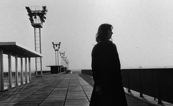 Movie still from “La Jetée” (1962), directed by Chris Marker – A woman standing on a pier in front of some lights; Medium shot, Low angle