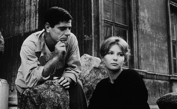 Movie still from “La Jetée” (1962), directed by Chris Marker – A man and a woman sitting next to each other on a couch; Medium shot, Low angle