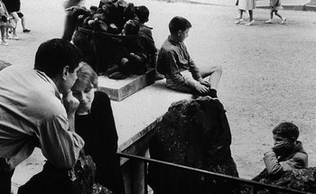 Movie still from “La Jetée” (1962), directed by Chris Marker – Black and white photograph of people sitting on a bench; Medium shot, High angle