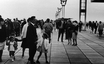 Movie still from “La Jetée” (1962), directed by Chris Marker – A black and white photo of people walking on a sidewalk; Extreme Wide shot, Low angle