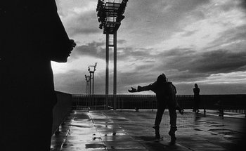 Movie still from “La Jetée” (1962), directed by Chris Marker – A person standing in the rain near a fence; Wide shot, Low angle