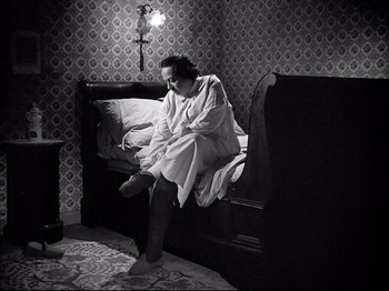 Movie still from “La Poison” (1951), directed by Sacha Guitry – A woman sitting on the edge of a bed in a bedroom; Medium shot, High angle