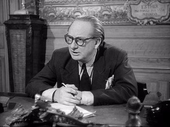 Movie still from “La Poison” (1951), directed by Sacha Guitry – An older man sitting at a table writing on a piece of paper; Medium shot, Low angle