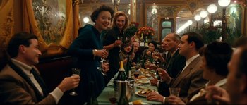 Movie still from “La Vie En Rose” (2007), directed by Olivier Dahan – A group of people sitting around a table with wine glasses; Medium shot, High angle