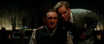 Movie still from “La Vie En Rose” (2007), directed by Olivier Dahan – A man and a man in a suit posing for a picture; Medium shot, Low angle