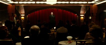 Movie still from “La Vie En Rose” (2007), directed by Olivier Dahan – A man standing on a stage in front of a group of people; Wide shot, Low angle