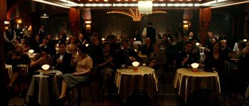 Movie still from “La Vie En Rose” (2007), directed by Olivier Dahan – A group of people sitting at a table in a room; Wide shot, High angle