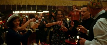 Movie still from “La Vie En Rose” (2007), directed by Olivier Dahan – A group of people standing in a room with drinks; Medium shot, Over the shoulder angle