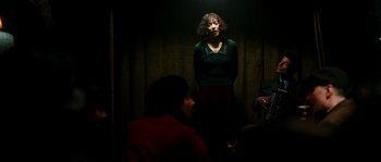 Movie still from “La Vie En Rose” (2007), directed by Olivier Dahan – A woman standing in the dark with a microphone; Medium shot, Low angle