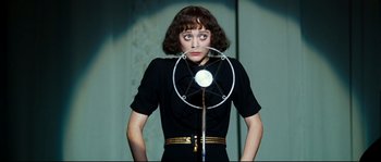 Movie still from “La Vie En Rose” (2007), directed by Olivier Dahan – A woman standing in front of a microphone; Medium shot, Low angle
