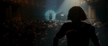 Movie still from “La Vie En Rose” (2007), directed by Olivier Dahan – A woman standing in front of an audience in front of a piano; Wide shot, Over the shoulder angle