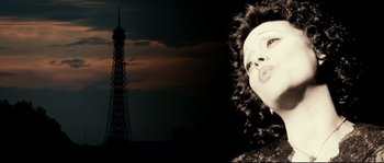 Movie still from “La Vie En Rose” (2007), directed by Olivier Dahan – A woman in a black and white photo near a tall tower; Close Up shot, Low angle