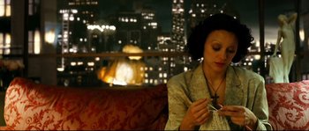 Movie still from “La Vie En Rose” (2007), directed by Olivier Dahan – A woman sitting on top of a red couch in front of a city skyline; Close Up shot, High angle