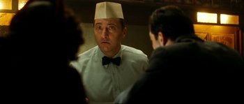 Movie still from “La Vie En Rose” (2007), directed by Olivier Dahan – A man wearing a paper hat in front of two other men; Close Up shot, Over the shoulder angle