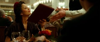 Movie still from “La Vie En Rose” (2007), directed by Olivier Dahan – Two people are sitting at a table and one person is holding a menu; Medium shot, Over the shoulder angle
