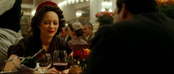 Movie still from “La Vie En Rose” (2007), directed by Olivier Dahan – A woman sitting at a table with a glass of wine; Close Up shot, Over the shoulder angle
