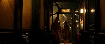 Movie still from “La Vie En Rose” (2007), directed by Olivier Dahan – A man and a woman standing in front of a fire exit sign; Wide shot, High angle