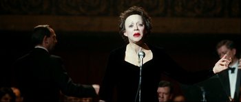Movie still from “La Vie En Rose” (2007), directed by Olivier Dahan – A woman in a black dress standing at a microphone; Medium shot, Low angle