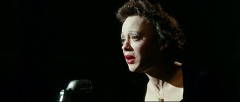Movie still from “La Vie En Rose” (2007), directed by Olivier Dahan – An older woman is speaking into a microphone; Close Up shot, High angle