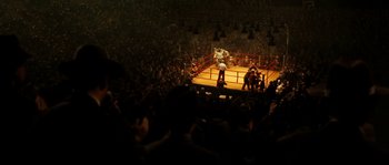 Movie still from “La Vie En Rose” (2007), directed by Olivier Dahan – A boxing ring with a crowd of people watching it; Extreme Wide shot, High angle